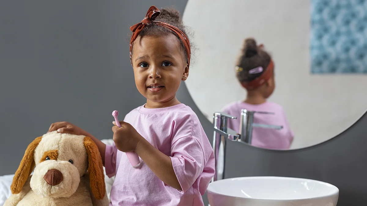 A very cute toddler with a doggy teddy bear sitting on the sink and holding issa 4 baby 